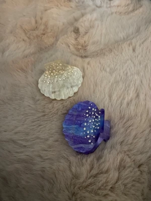 Snäck klämmor i olika färger - Två mindre snäck klämmor, en vit och en lilla/blå och båda har vita stenar på sig. De är väldigt fina har  aldrig använt för jag passar inte så bra i klämmor.  