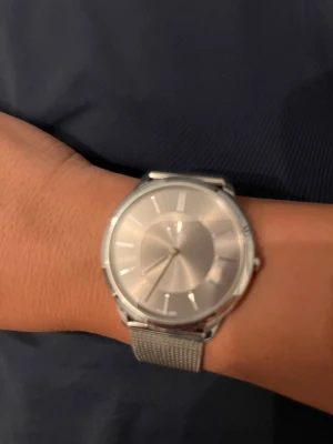 Silverfärgad klocka från Calvin Klein - Stilren klocka från Calvin Klein i helsilver med mesh-armband i metall. Minimalistisk urtavla utan siffror och diskreta indexmarkeringar. Perfekt accessoar för dig som gillar en clean och modern look.