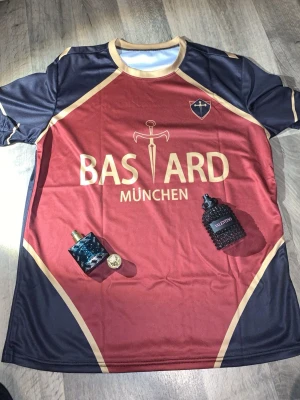 Bastard München Isagi 11 matchtröja - Cool matchtröja från Bastard München med Isagi 11 på ryggen. Tröjan är vinröd och svart med guldiga detaljer och tryck, tillverkad i ett lätt och snabbtorkande material som passar perfekt till fotboll eller träning. Snygg design med klubbmärke och svärd på bröstet.