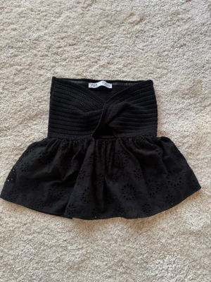 Svart broderad topp från Zara - Supersnygg svart topp från Zara med twistad, ribbad överdel och broderad volang nertill. Toppen är ärmlös och har en croppad passform som ger en trendig look. Perfekt att styla med höga jeans eller kjol. Inte använd. 