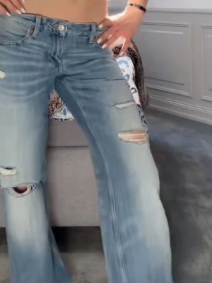 Ljusblå slitna bootcut jeans - Säljer dessa populära jeans från Zara som just nu är slut sålda (jeans trf wide leg låg midja) flera slitningar och hål på benen. Jeansen har klassisk femficksmodell, låg midja och är tillverkade i denim. Perfekta för en avslappnad och trendig look. Säljer pågrund över att jag inte var nöjd med passformen! (HELT NYA MED PRISLAPP)