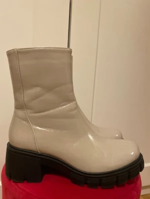 Beiga stövletter med dragkedja - Säljer ett par beiga stövletter med svart sula. Skorna har glansig finish och dragkedja på insidan för enkel påtagning. 💗