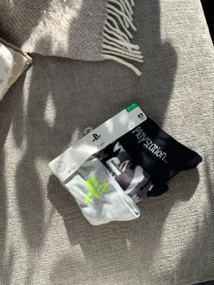Playstation strumpor 3-pack NY! - 3-pack Playstation strumpor i svart, grått och vitt. Ena paret är helsvart med Playstation-logga, ett par är grå med neongrön logga och ett par har ett camomönster i svart, vitt och grått. Perfekta för dig som gillar gaming och snygga detaljer.