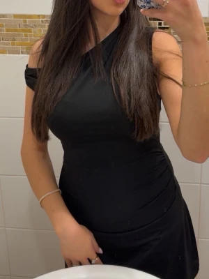 Svart oneshoulder klänning - Snygg svart oneshoulder klänning med figurnära passform. Klänningen har en stilren design och är perfekt för dig som vill ha en enkel men elegant look. Materialet känns mjukt och följsamt mot kroppen.