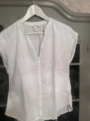 Vit blus från H&M - Säljer en vit, luftig blus från H&M i storlek XS. Blusen har en avslappnad passform, v-ringning och korta ärmar. Tillverkad i ett tunt, svalt tyg som passar perfekt till sommaren. Enkel och stilren design som är lätt att matcha.