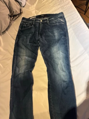 Blå Replay Anbass jeans slim fit - Säljer ett par blå Replay Anbass jeans i storlek 36 med slim fit. Jeansen har klassisk femficksmodell, snygga slitningar och kontrastsömmar. Materialet är denim med stretch för extra komfort. Perfekta för dig som gillar en modern och avslappnad stil.