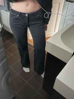 Svarta raka jeans med låg midja - Säljer ett par svarta jeans med låg midja och raka ben. Klassisk femficksmodell med silverfärgade knappar och nitar. Jeansen har en enkel och stilren look, perfekta till en avslappnad outfit. Materialet är denim i bomull.