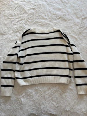Randig stickad tröja  - Säljer en vit stickad tröja med svarta horisontella ränder. Tröjan har rund halsringning, långa ärmar och ribbade muddar vid ärmslut och nederkant. Storlek XS.
