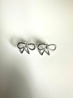 Söta silvriga rosettörhängen - helt NYA - Ett par HELT NYA små örhängen i form av rosetter i silverfärgad metall. De har en enkel och stilren design som ger en gullig touch till din look. Perfekta för dig som gillar detaljer och vill ha något diskret men ändå unikt. Nya i förpackning, då jag fick dubbelt. 