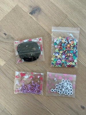 Pärlkit med elastisk tråd - Säljer ett komplett pärlkit med färgglada plastpärlor i olika former och storlekar, elastisk smyckestråd från Crystal Tec (0.7 mm) samt svarta och vita snören. Perfekt för att skapa egna armband, halsband eller andra smycken.