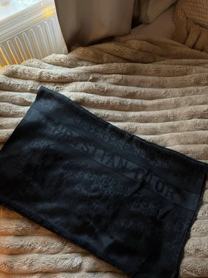Svart sjal från Christian Dior - Snygg svart sjal från Christian Dior med diskret logomönster och bredare band där märkesnamnet syns tydligt. Tillverkad i ett mjukt tyg som känns lyxigt och passar perfekt till att lyfta vilken outfit som helst. Ny pris 7500kr