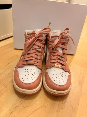 Air Jordan 1 Mid rosa och vit - Ny pris 2000.Snygga Air Jordan 1 Mid sneakers i rosa och vitt läder med klassisk guldfärgad Swoosh och Jordan Wings-logga på sidan. Skorna har perforerad tå, matchande rosa skosnören och en vit mellansula. Perfekt för dig som vill ha en ikonisk och trendig look. Använda typ 3 gånger. 