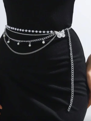 Bälte midja kedja Silvrigt kedjebälte med pärlor & fjäril - Trendigt silvrigt kedjebälte med flera lager, dekorerat med vita pärlor och en söt fjärilsdetalj. Perfekt för att lyfta en enkel outfit och ge den extra edge. Justerbar längd för att passa olika stilar.