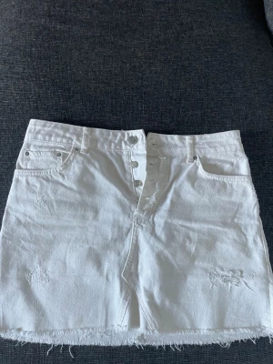 Vit jeanskjol från Zara - Cool vit jeanskjol med rå kant och slitningar. Kjolen har knappar framtill, fickor både fram och bak samt en kort passform. Perfekt för dig som gillar en avslappnad och trendig stil. Materialet är klassisk denim och kjolen har en enkel, stilren look. Passar även mig som vanligtvis har storlek S🩷