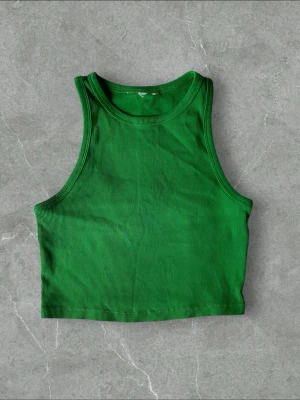 Grön ribbad croppad linnetopp - Snygg grön croppad linnetopp med ribbad struktur. Toppen är ärmlös och har en klassisk rund halsringning. Perfekt att styla med höga jeans eller kjol för en trendig look.