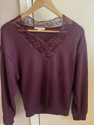 Vinröd stickad tröja med spets - Mysig vinröd stickad tröja från Gina Tricot med v-ringning och dekorativ spetsdetalj runt halsen. Tröjan har långa ärmar och en avslappnad passform. Perfekt för dig som gillar en feminin touch på din stickade garderob.