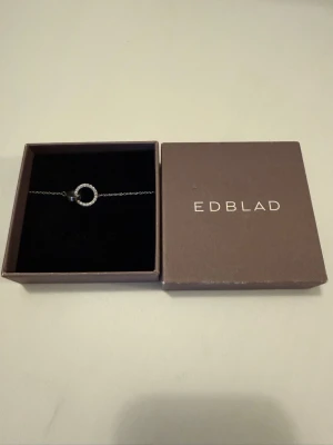 Silverhalsband med cirkel från Edblad - Snyggt silverfärgat halsband från Edblad med en tunn kedja och en rund cirkelberlock dekorerad med små gnistrande stenar. Kommer i original ask. Perfekt accessoar för att lyfta din outfit.