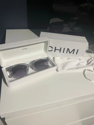Chimi transparenta solglasögon - Snygga solglasögon från Chimi med transparent båge och mörka glas. Klassisk fyrkantig form som passar till många stilar. Kommer med originalfodral och putsduk. Perfekta för soliga dagar och ger en cool vibe.