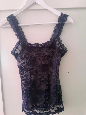 Mörkblå spetslinnetopp - Säljer en mörkblå, ärmlös linnetopp i genombruten spets med blommigt mönster. Toppen har breda spetsband och en feminin, figurnära passform. Perfekt att styla lager på lager eller som den är för en trendig look.