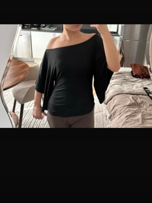 Svart offshoulder topp - Snygg svart offshoulder topp med vida trekvartsärmar. Tunn och mjuk i materialet, perfekt för en trendig och avslappnad look. Passar till både jeans och kjol för en cool stil.