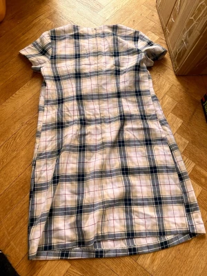 Rutig kortärmad klänning i bomull - Supersöt kortärmad klänning med rutigt mönster i vitt, blått och beige. Klänningen har en rak passform och är tillverkad i mjuk bomull, perfekt för en avslappnad och trendig look. Dragkedja i ryggen för enkel på- och avtagning.Skriv gärna för mått! 💕