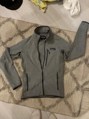 Grå Patagonia fleece - Säljer en riktigt snygg Patagonia fleece som är perfekt nu till våren/sommaren. Den är i riktigt fint skick och nypris kostar den 1500kr. Storleken är XXS och passar mellan 150-163 cm lång kille. Skriv för minsta fundering!