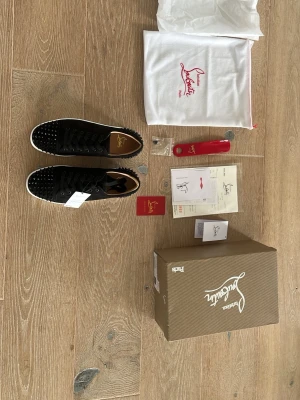 Svarta Louboutin sneakers med nitar - Snygga svarta sneakers från Christian Louboutin med svarta nitar på tå och häl. Skorna har svart mocka. Allt på bilden ingår, även äkthetsärtifikat från Vinted. Tveka inte på att ställa frågor.