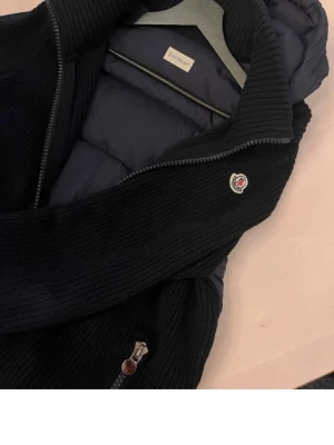 Mörkblå dunväst från Moncler - Snygg mörkblå dunväst från Moncler med stickade detaljer och dragkedja framtill. Västen har Moncler-logga på bröstet och quiltad design som ger en cool look. Perfekt för lager-på-lager och håller dig varm under kyliga dagar.