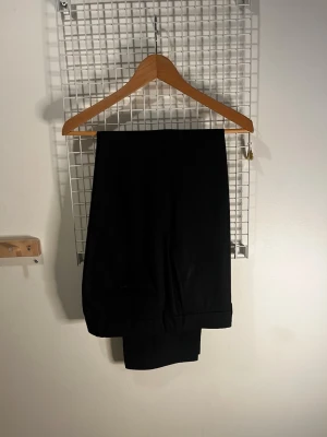 Svart kostym - Snygga svarta kostymbyxor med rak passform, pressveck och bakficka med knapp. Byxorna har skärphällor och är tillverkade i ett slätt tyg som troligen är en blandning av polyester och viskos. Perfekta för en clean och dressad stil.