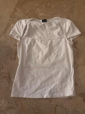 Vit basic t-shirt från Gina Tricot - En klassisk vit t-shirt från Gina Tricot i mjuk bomull. Modellen har korta ärmar och rund halsringning. Perfekt att matcha med jeans eller kjol för en enkel och clean look.