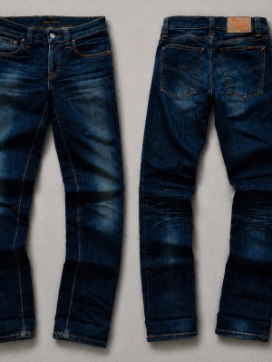 Mörkblå jeans från Nudie Jeans - Säljer ett par mörkblå jeans från Nudie Jeans med snygga slitningar och kontrastsömmar. Klassisk femficksmodell med läderpatch bak och vågdetalj på bakfickan. Tillverkade i denim med en schysst tvättad look. Kan sänka priset vid snabb affär.