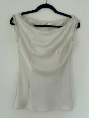 Vit ärmlös linnetopp - Snygg vit linnetopp med enkel och clean design. Toppen är ärmlös och har en rak passform med diskret båtringad hals. Perfekt för varma dagar och enkel att styla med olika accessoarer.