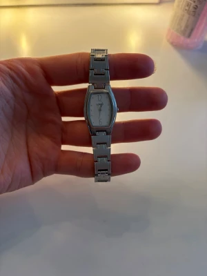 Silverfärgad klocka från Lorus - Stilren klocka från Lorus med silverfärgat armband i metall och vit urtavla. Klockan har en avlång, något rektangulär form och klassisk design. Perfekt accessoar för dig som gillar en tidlös look.