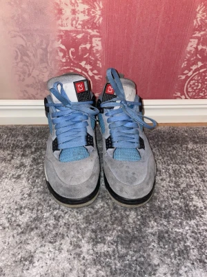 Air Jordan 4 University Blue (41) - Snygga Air Jordan 4 University Blue med blå mocka och mesh, svarta detaljer och specklad grå sula. Klassisk Jumpman-logga på plösen och coola plastdetaljer vid snörningen. Perfekta för dig som gillar streetwear och vill sticka ut med dina sneakers.