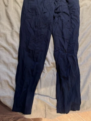 Mörkblå mjukisbyxor Vero Moda - Mörkblå linnebyxor från Vero Moda med resår i midjan och dragsko. Byxorna har raka ben och är tillverkade i ett mjukt och bekvämt tyg, perfekta för en avslappnad stil.