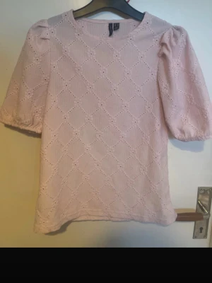 Ljusrosa blus med puffärm från H&M - Söt ljusrosa blus från vero Moda med puffärmar och broderade detaljer i ett diskret mönster. Blusen har rund halsringning och är tillverkad i bomull, vilket gör den både bekväm och luftig. Perfekt för dig som gillar romantisk och feminin stil.