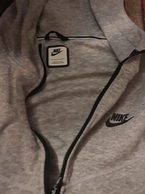 Grå zip hoodie från Nike - Säljer en grå hoodie från Nike med dragkedja framtill och två svarta dragkedjeförsedda fickor. Klassisk Nike-logga på bröstet och huva med snörning. Perfekt för chill eller träning, riktigt skön och enkel att matcha. L storlek och kan passar M också