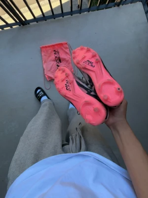 Nike Zoom Mercurial fotbollsskor - Nike Zoom Mercurial fotbollsskor med vit ovandel, svart swoosh och neonrosa dobbsula. Skorna har snörning och levereras med en rosa Nike-påse. Designade för snabbhet och bra grepp på planen, perfekta för dig som vill sticka ut.