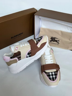 Burberry beige och bruna sneakers - Snygga sneakers från Burberry med klassiskt rutigt mönster i svart, vitt och beige. Skorna har detaljer i brunt och ljusrosa samt en bred rem med Burberry-logga över foten. Ovandelen är i en mix av läder och textil, och sulan är vit och chunky.