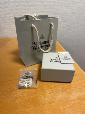 Vivienne Westwood pärlhalsband - Snyggt halsband från Vivienne Westwood med vita pärlor och det ikoniska orb-hänget i silverfärg. Kommer med originalförpackning, påse och tagg. Perfekt statement-piece för dig som gillar trendiga accessoarer.