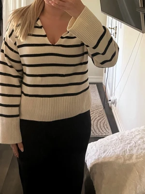 Randig stickad tröja med v-ringning - Säljer en krämvit stickad tröja med svarta horisontella ränder. Tröjan har v-ringad hals, breda ribbade muddar och avslappnad passform. 💗