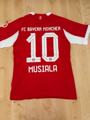 Musiala #10 – Player Edition (storlek M) - Musiala #10-tryck. Player Edition. Storlek M. Helt ny och aldrig använd. Säljs i befintligt skick. Skickas snabbt! 🚚💨  Mått för denna tröja (storlek M): (Uppmätta av leverantör – viss variation kan förekomma) • Halva bröstmåttet: 51 cm • Tröjans längd: 72,5 cm • Ärmbredd: 22,5 cm • Axelbredd: 43 cm • Ärmlängd: 39 cm • Manschettbredd: 18 cm  🔥 Player Edition-modell – tajtare passform än vanliga supportertröjor.