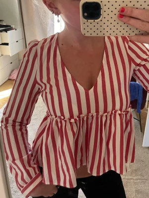 Röd- och vitrandig blus med v-ringning - Snygg blus med röda och vita vertikala ränder, djup v-ringning och volang nedtill. 