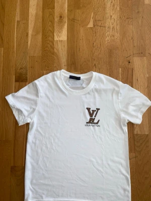L och V - Snygg vit t-shirt från  med klassisk  på bröstet. T-shirten har rund hals och korta ärmar, perfekt för en clean och stilren look. Tillverkad i mjuk bomull som känns skön mot huden.