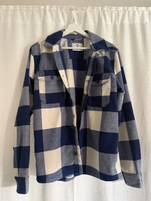 Blåvit rutig overshirt från C - Overshirt i blåvitt rutigt mönster från C. Skjortan har två bröstfickor med lock och knappar, klassisk krage och knäppning framtill. Perfekt lager-på-lager-plagg med avslappnad passform och långa ärmar. Materialet känns mjukt och slitstarkt.