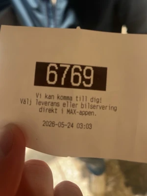 Nummerlapp från MAX 6769 - En vit nummerlapp från MAX med svart tryck och numret 6769 i stort format. Texten informerar om leveransalternativ via MAX-appen och datumet 2026-05-24 är utskrivet längst ner. Perfekt för samlare av restaurangprylar eller som kul minne.