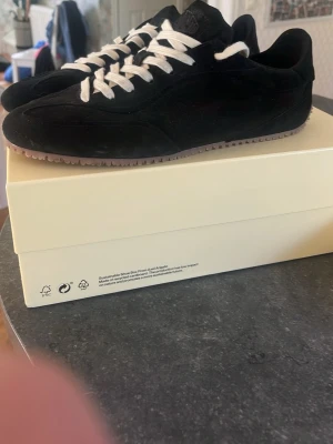 Svarta sneakers från Axel Arigato Daze runners  - Stilrena svarta sneakers från Axel Arigato i mocka med vita snören och diskret logga på sidan.  skorna är faktiskt aldrig använda då jag köpte dem och glömde lämna tillbaks. Skorna har en låg siluett och en klassisk gummisula i ljusbrunt. Perfekta för dig som gillar minimalistisk och modern design. Köpte från Minto och kvitto finns. Ny pris 2850