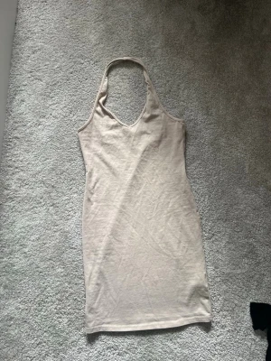 Halterneckklänning - Säljer en enkel och stilren beige klänning med halterneck och v-ringning. Perfekt för varma dagar och kan stylas på många olika sätt.