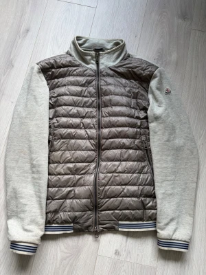 Maglia Cardigan - Grå hybridjacka från Moncler. Ärmarna har gått upp lite längst ner vid muddar (bild 4 & 5). Inget märkvärdigt vid användning och bör gå att sy igen vid intresse, därmed det sjukt billiga priset. Storlek L, då Moncler sitter något små i storlekar sitter denna nog mer som en M. 