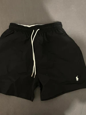 Polo Ralph Lauren Badshorts  - Svarta badshorts från Polo Ralph Lauren med en bakficka med lock. Perfekta för stranden eller sommaren. Storlek M men passar mer till S 